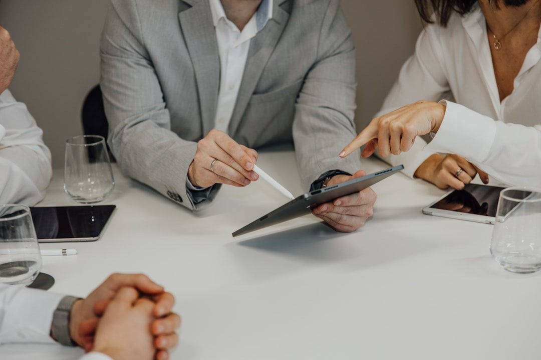Business professionals collaborating on a tablet at a white table.
